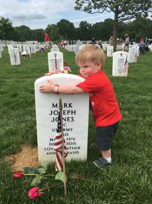 young child hugging a tombstone in a veteran cemetery